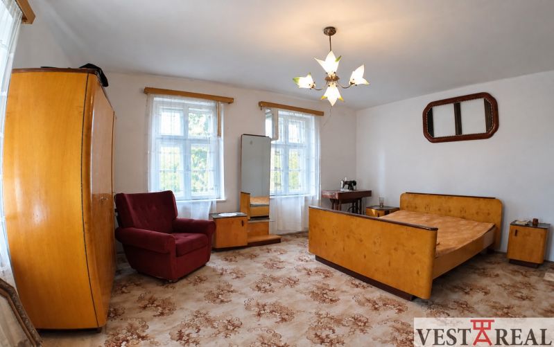 A room in a family house with older furniture, an upholstered armchair, and a floral carpet.
