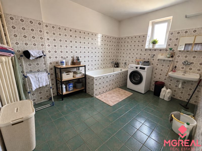 A bathroom in a family house with a washing machine, a bathtub, and green tiles.