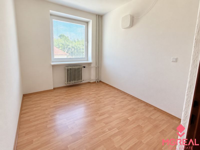 An empty room with a window, wooden floor, white walls, and a radiator.