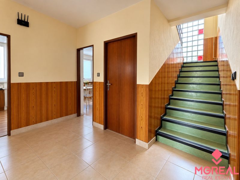 Interior of a family house with a staircase, light flooring, and wooden decor on the walls.