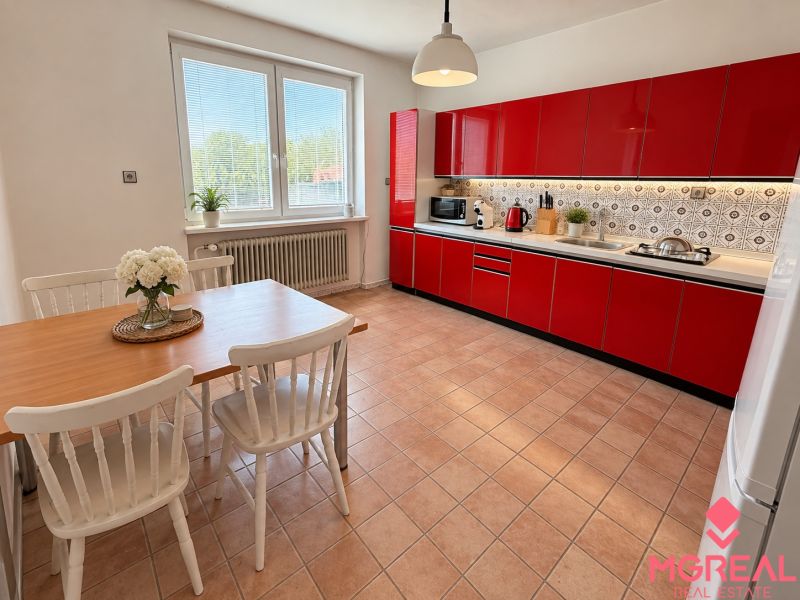 A kitchen in a family house with a red kitchen unit and a dining table for four.