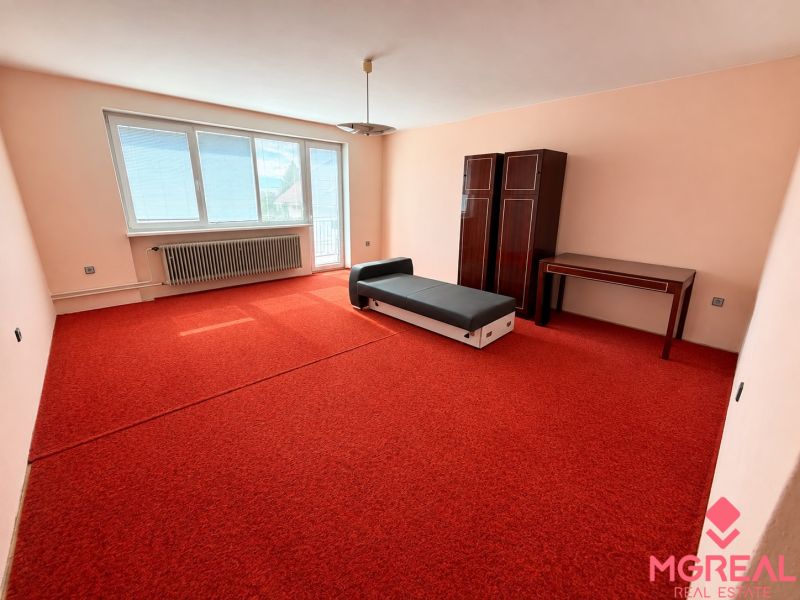 A room in a family house with a red carpet, simple furniture, and a large window.