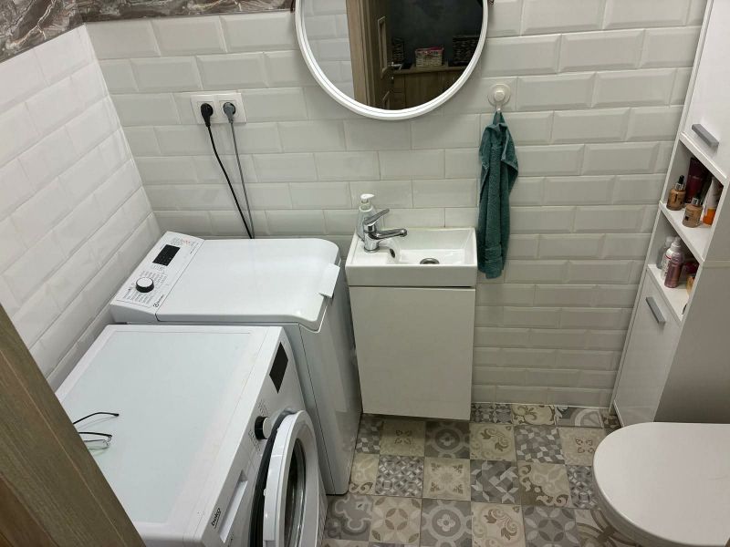Bathroom with a washing machine, sink, and toilet in a family house with a tiled floor.