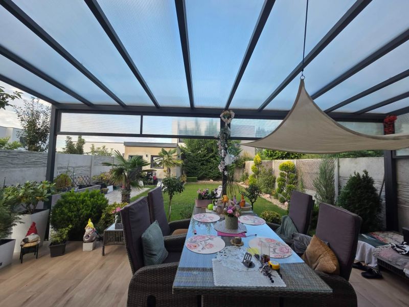A covered terrace with a dining table and a view of the garden in a family house.