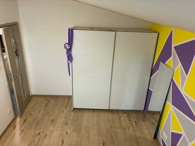 A room with a white wardrobe, a colorful wall, a wooden decor floor, and a toy.