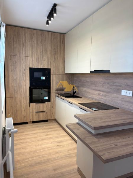 A kitchen in a 2-room apartment with a wooden decor floor and light furniture.