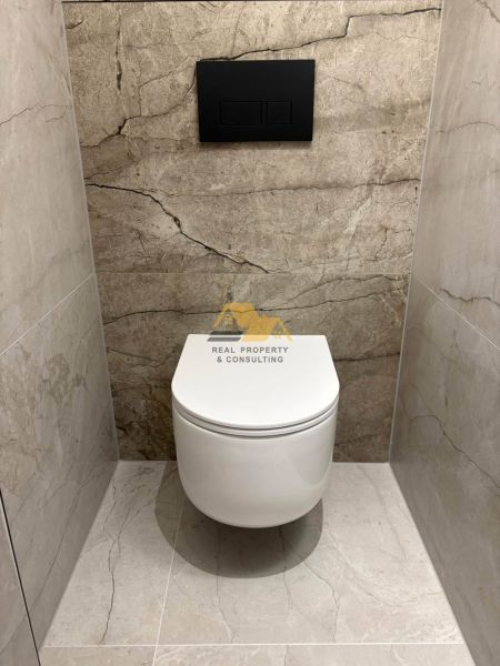 A toilet with a wall-hung WC and stone tiles in a 2-room apartment.