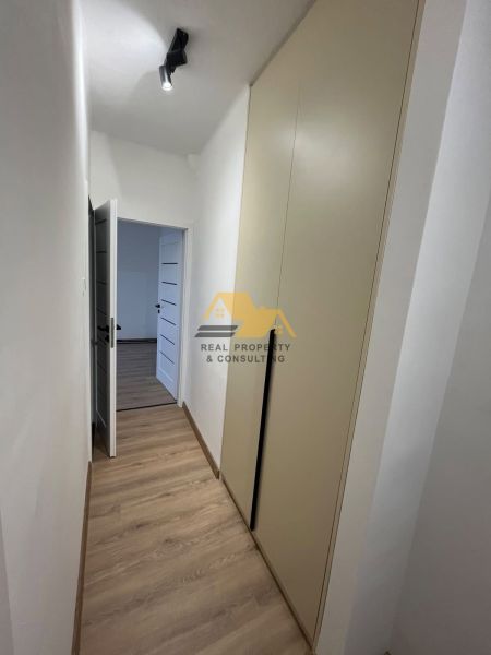 A narrow hallway with a wooden decor floor leading to a two-room apartment.