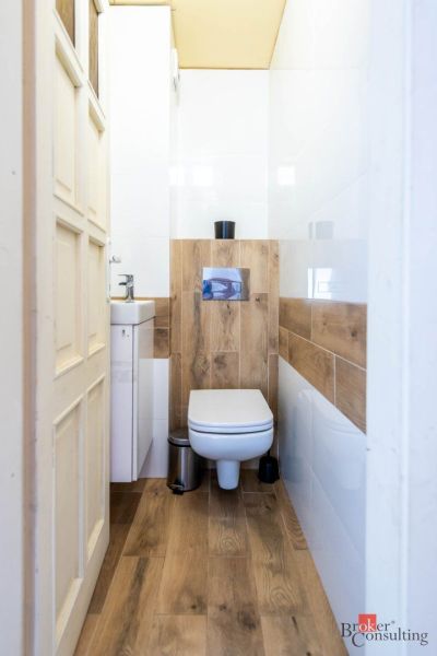 A toilet with a wooden decor floor, a small sink, and white walls.
