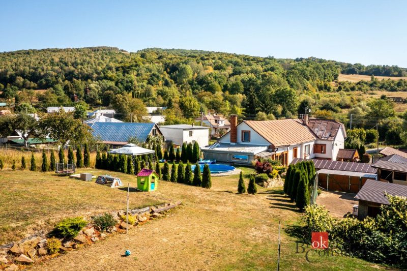A family house in Potoky, a garden with a swimming pool and lawn, surrounded by trees and hills.