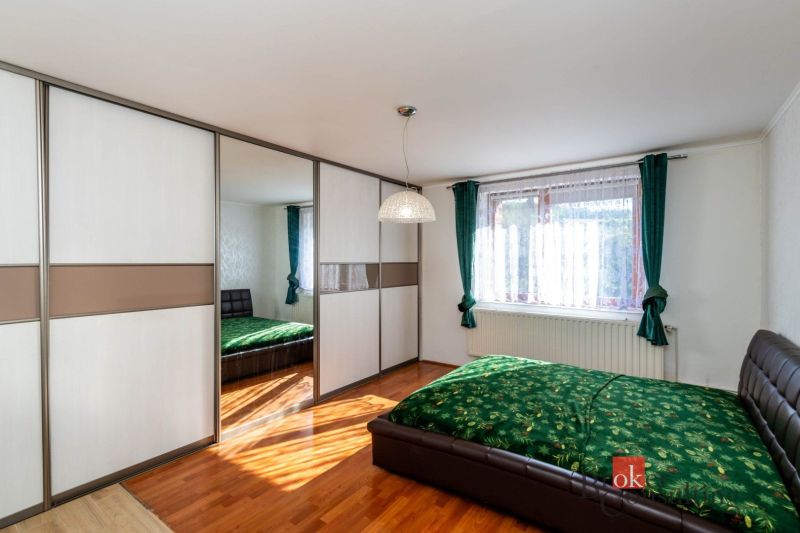 A bedroom in a family house with a sliding wardrobe, green curtains, and a wooden decor floor.