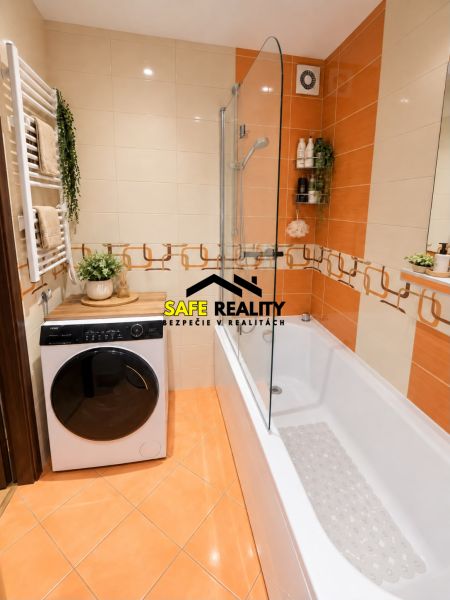 A bathroom with a shower and a washing machine in a 3-room apartment, warm orange tiles.