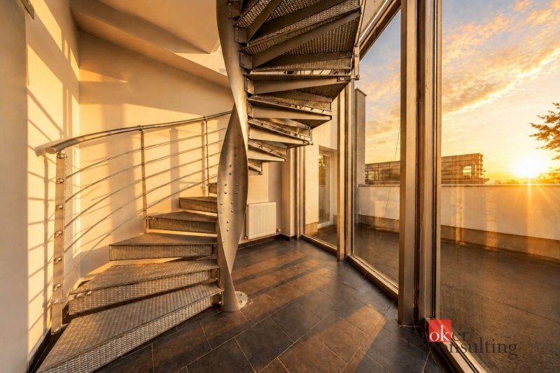 A villa with a spiral metal staircase and large windows overlooking the sunset.