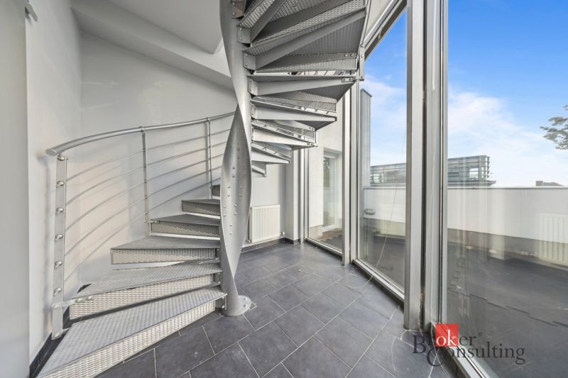 A spiral metal staircase next to large glass windows in the interior of a villa.
