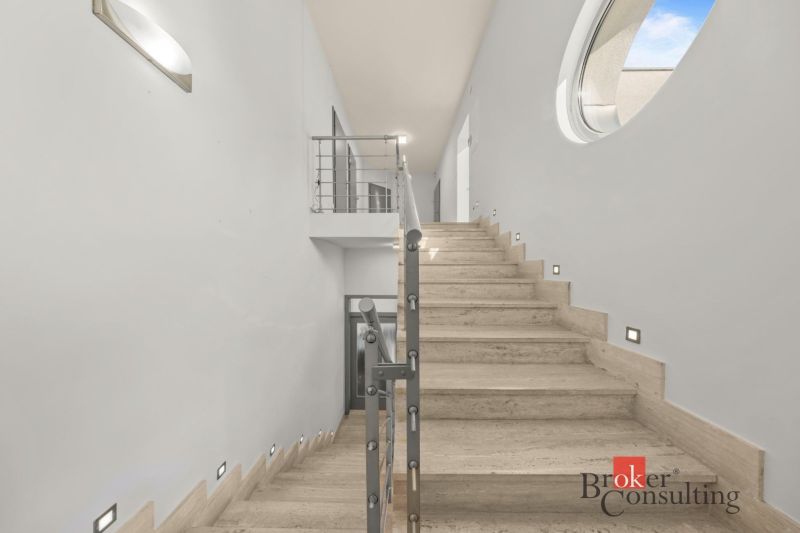 A staircase in a villa with marble steps and stainless steel railing.