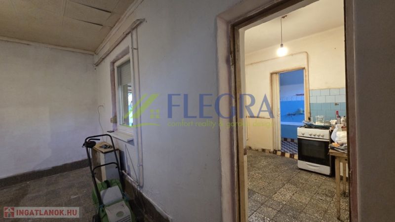 A family house with a kitchen, tiled floor, and a window, entrance to another room.