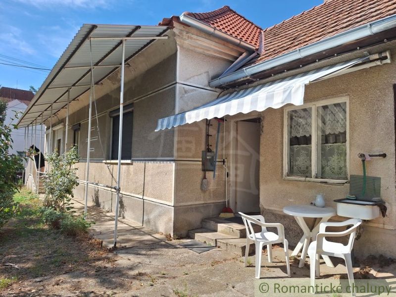 A family house in Moča with a terrace, table and chairs, white shelter, blue sky.
