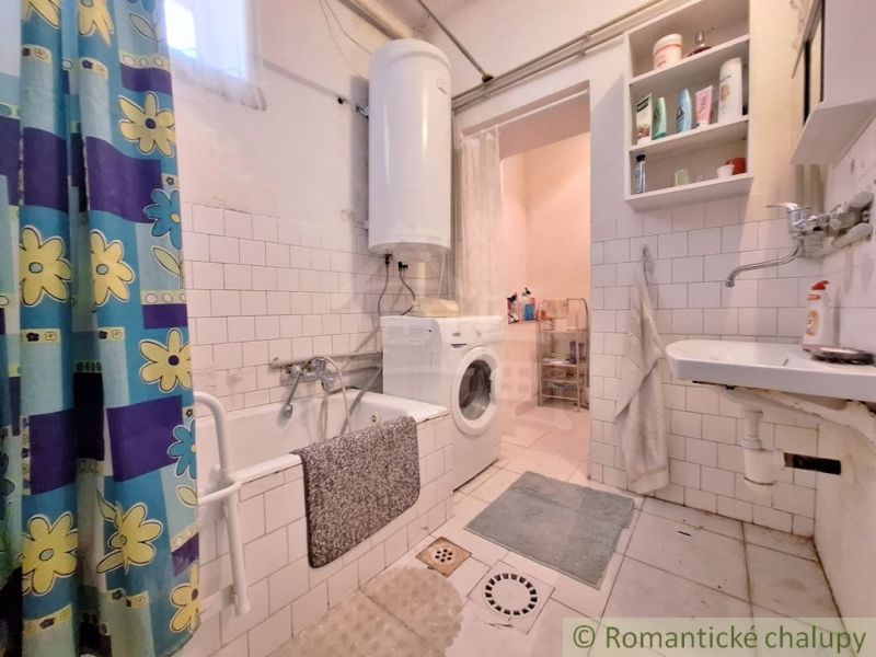 A bathroom in a family house with a bathtub, a sink, a washing machine, and white tiles.