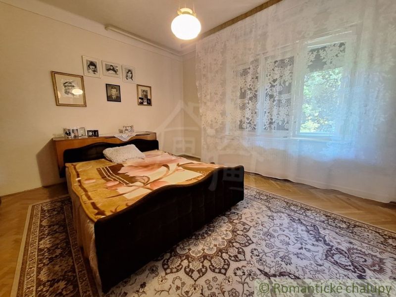 Bedroom in a family house with a bed, curtains, carpet, and wooden decor flooring.