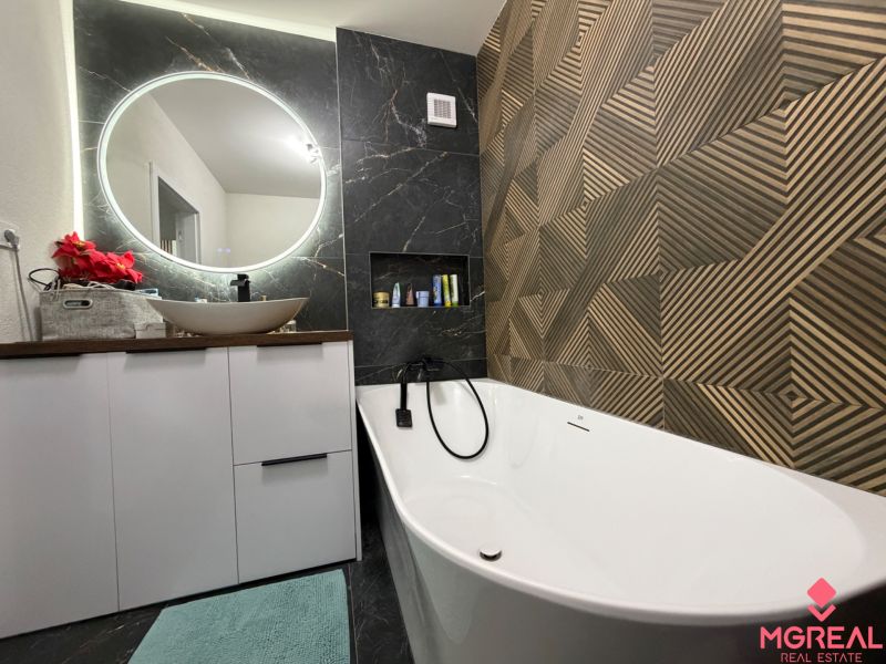 A bathroom in a 3-room apartment with a round mirror, a bathtub, and a decorative wall.