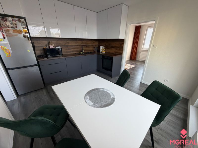 A kitchen in a 3-room apartment with a wooden decor floor, green chairs, white table.