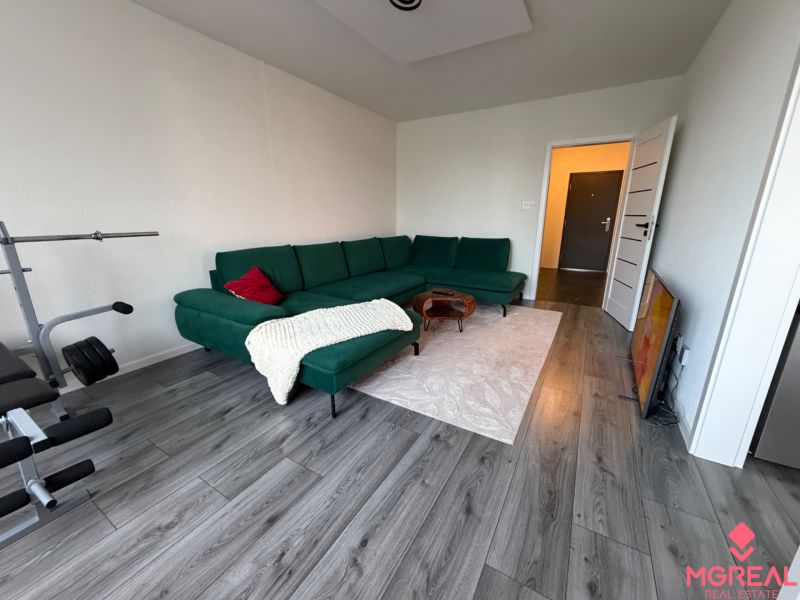 Living room of a three-room apartment with a wooden decor floor and a green sofa.