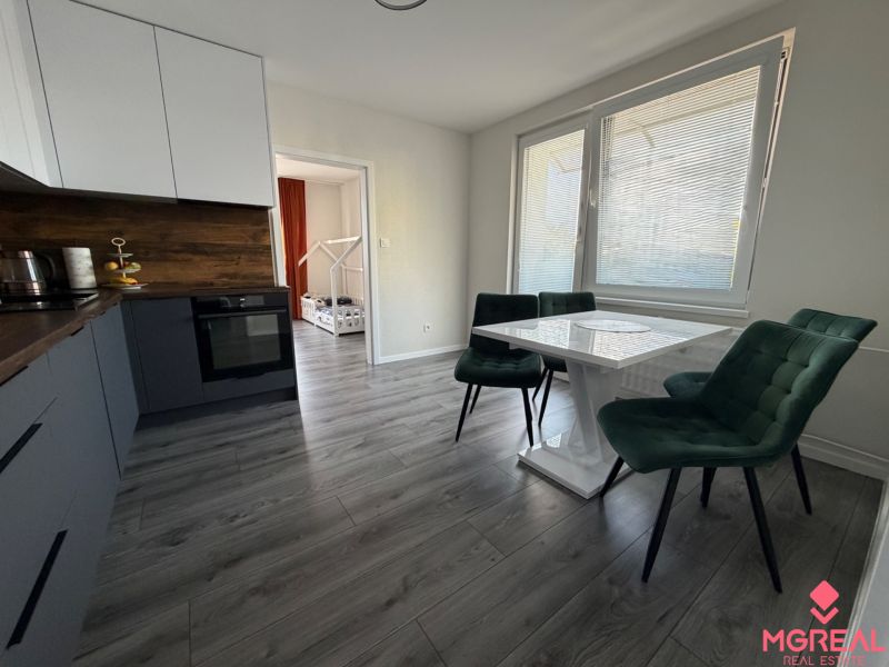 A bright kitchen with a dining table, wooden decor flooring, and an open passage to a room in a 3-room apartment.