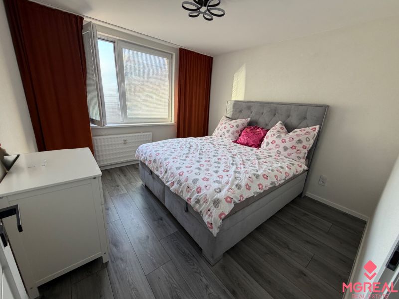 A bedroom with a bed and a wooden decor floor in a three-room apartment.
