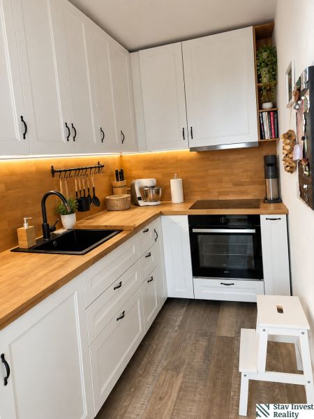 A kitchen with white cabinets, a wooden countertop, and a floor with a wooden decor in a 3-room apartment.