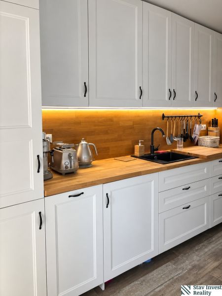 A kitchen with white cabinets, wooden decor, and underlighting in a 3-room apartment.