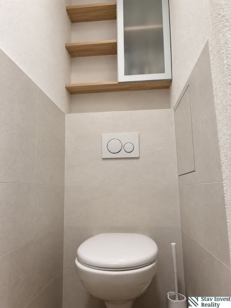 A toilet with a wall-mounted bowl, shelves, and a cabinet in a 3-room apartment.