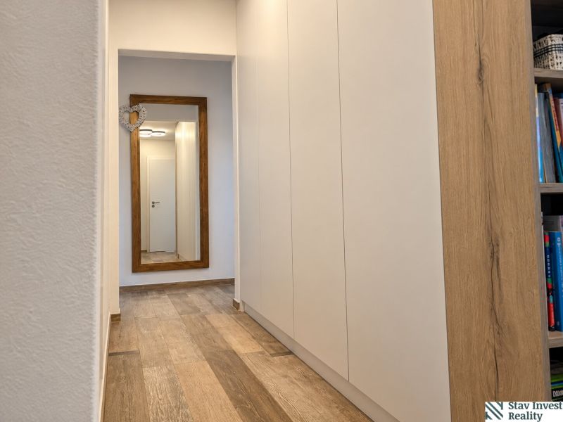 A hallway in a 3-room apartment with a wooden decor floor and a large mirror.