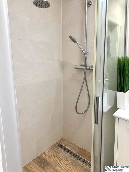 Shower corner in a 3-room apartment with a wooden decor floor and glass doors.