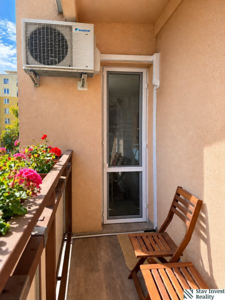 A balcony in a 3-room apartment with air conditioning, wooden chairs, and flowers.