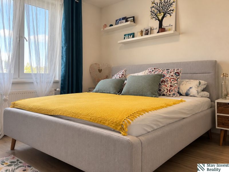 A bright bedroom with a bed, yellow blanket, shelves, and a wooden decor floor in a 3-room apartment.