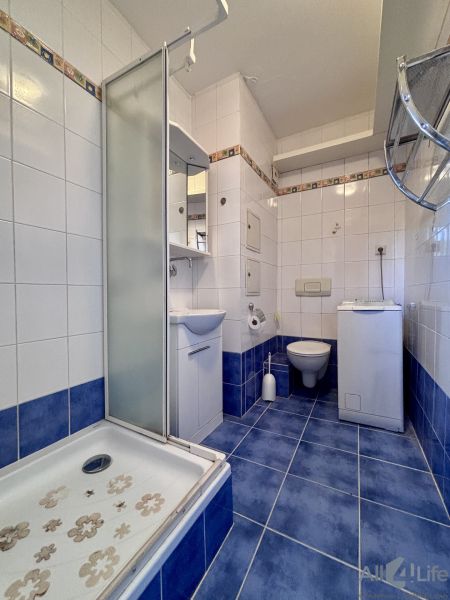 A bathroom with blue tiles, a shower, a sink, a washing machine, and a toilet in a 2-room apartment.