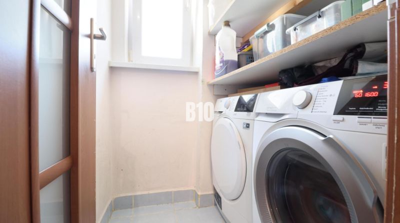 Washing machine, dryer, and shelves with cleaning products in the laundry room of a three-room apartment.