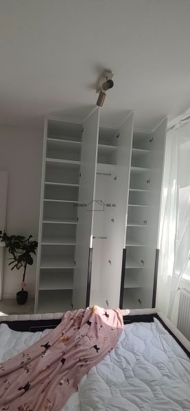 An open white wardrobe in a 3-room apartment with blankets on the bed.