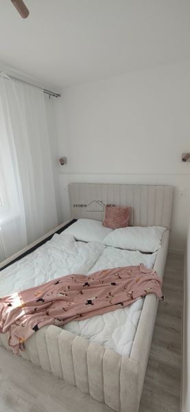 Bedroom in a 3-room apartment with a bed on the floor with a wooden decor, white wall, and curtain.