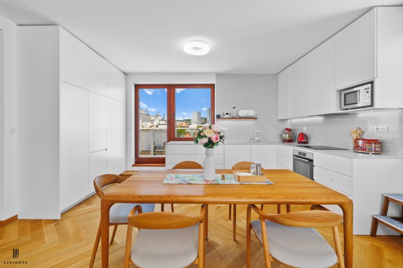 A kitchen of a three-room apartment with a wooden decor, white cabinets, and a window with a view.
