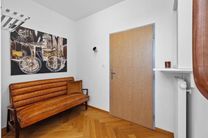 A hallway in a 3-room apartment with a painting, a sofa, and a wooden decor floor.