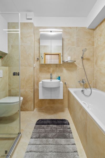 A bathroom in a three-room apartment with a bathtub, shower corner, and tiles in cream tones.