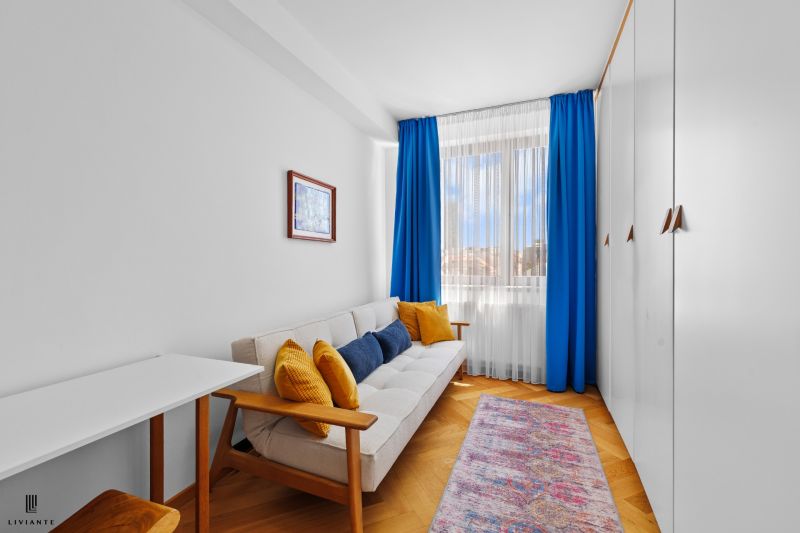 A bright room with blue curtains, a sofa, a carpet, a wardrobe, and a wooden decor floor.