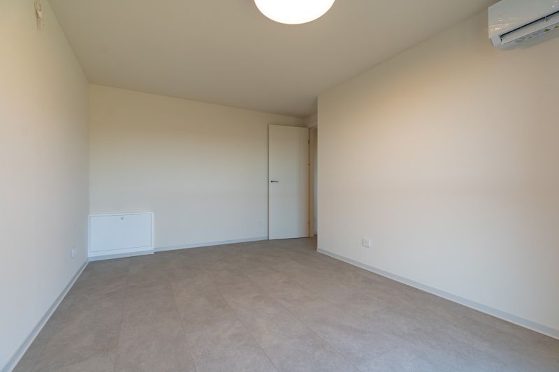 An empty room in a 4-room apartment with beige walls and air conditioning.