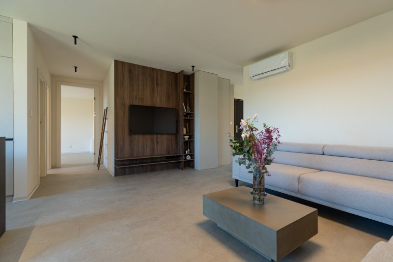 Living room with a gray sofa, flowers on the table, and a TV on a wooden wall.
