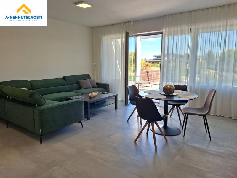 A bright living room with a large sofa, dining table, and a view outside in a two-room apartment.