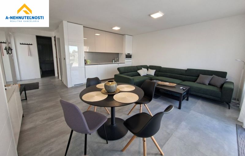 Living room with a kitchenette in a two-room apartment, featuring a dark sofa and a round table.