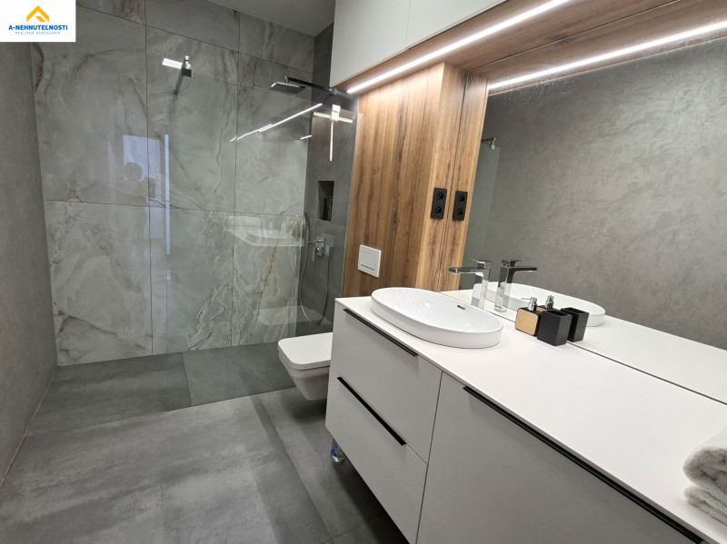 A bathroom with a large mirror, a shower, and a sink in a two-room apartment.