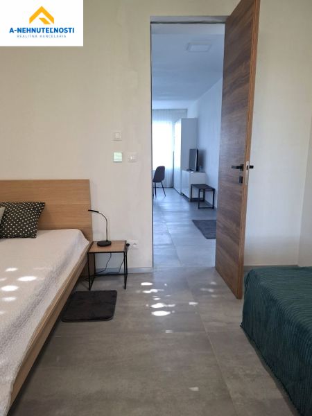 Bedroom with a bed and a view into the living room in a 2-room apartment, with a wooden decor floor.