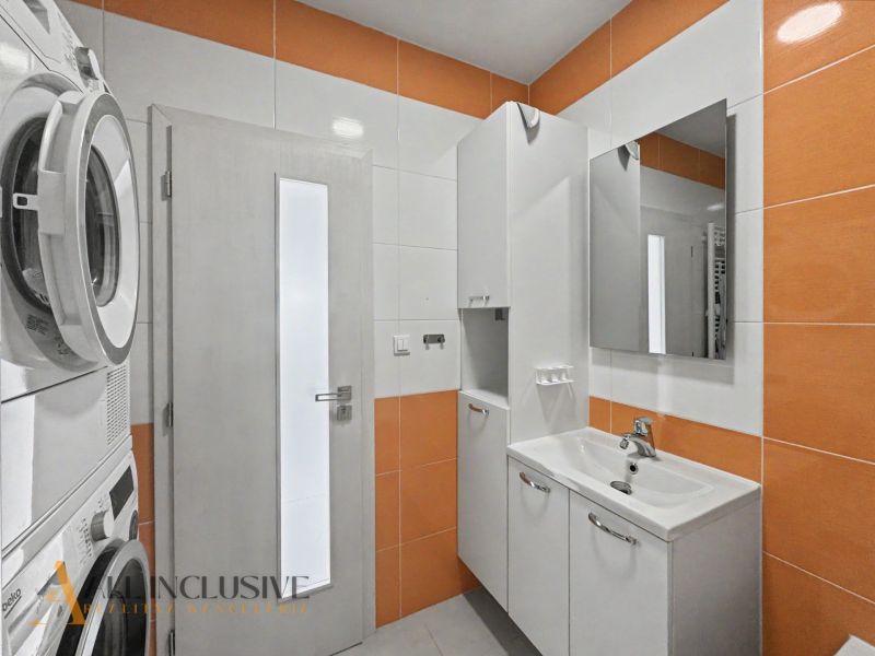 A bathroom in a 2-room apartment with a washing machine, dryer, and sink, white with orange elements.